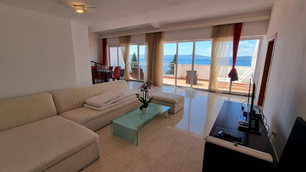 Jasny salon z kremową kanapą i nowoczesnymi kafelkami. Wspaniały widok na morze.