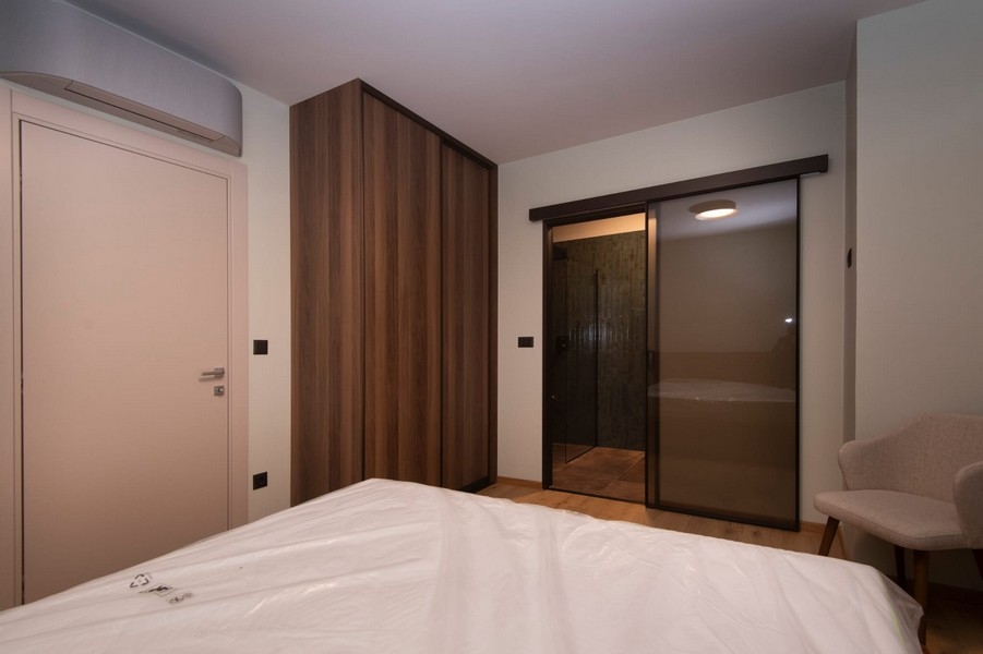 Sypialnia z bezpośrednim dostępem do łazienki w nowoczesnym mieszkaniu na sprzedaż w Splicie w Chorwacji, z dużym łóżkiem i eleganckimi meblami.