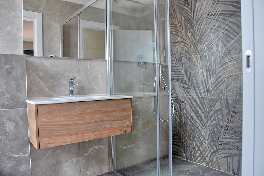 Nowoczesna łazienka w apartamencie na Istrii z kabiną prysznicową z ozdobnymi szklanymi płytkami i drewnianą szafką podumywalkową.