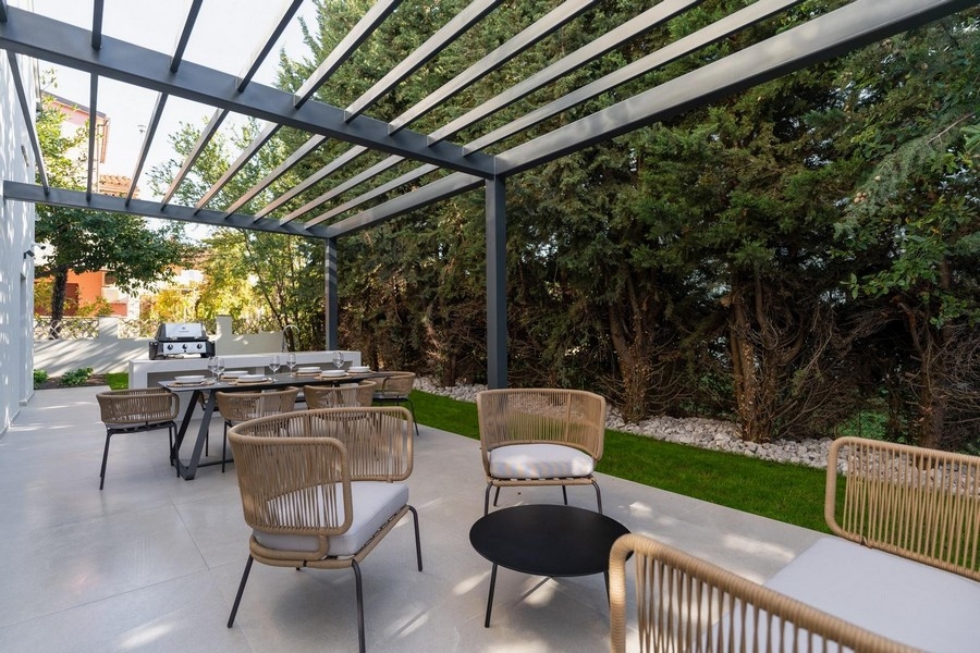 Widok zewnętrzny na taras z letnią kuchnią i jadalnią w luksusowym apartamencie na Istrii, otoczonym zielenią