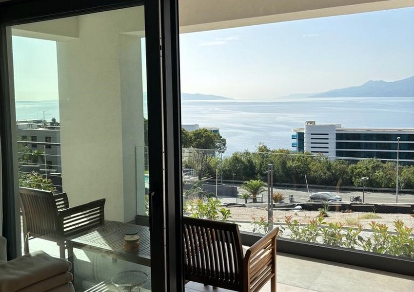 Balkon z drewnianymi krzesłami i widokiem na morze przez otwarte szklane drzwi, wykaz nieruchomości w Rijece, Chorwacja.