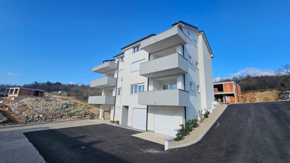 Widok z zewnątrz białego apartamentowca na sprzedaż w Crikvenicy w Chorwacji, z miejscem parkingowym i czystym błękitnym niebem