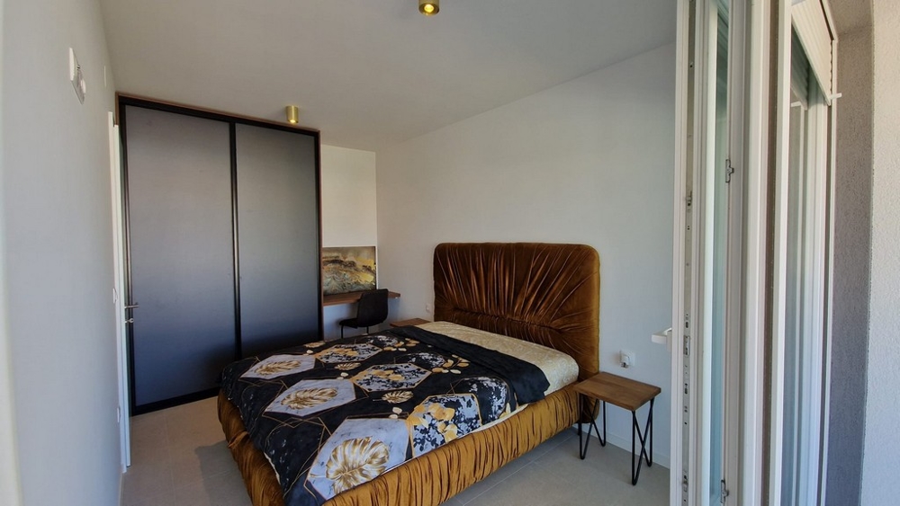 Sypialnia mieszkania w Novalji na wyspie Pag, z brązowym łóżkiem i dostępem do balkonu, nieruchomość w Chorwacji