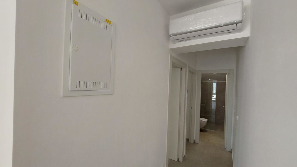 Widok wnętrza pustego pokoju z podłogą wyłożoną kafelkami, dużymi oknami i kilkoma drzwiami