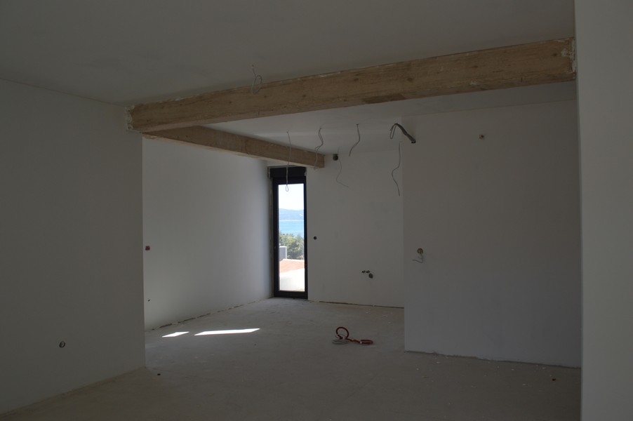Przestronny salon w niedokończonym mieszkaniu z odsłoniętymi belkami stropowymi i widokiem na morze.