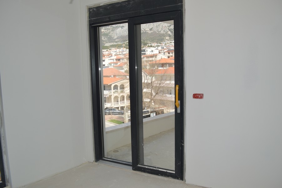 Drzwi balkonowe w niewykończonym mieszkaniu z widokiem na okoliczne domy i góry.