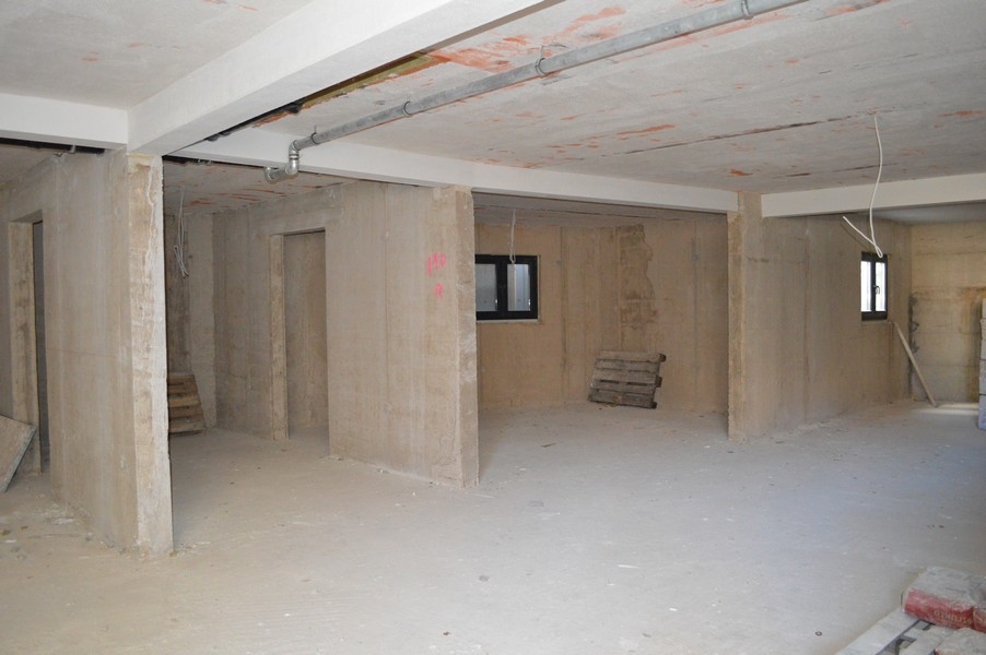 Niewykończone pomieszczenie piwniczne z betonowymi ścianami i podłogami przeznaczone na miejsca parkingowe.