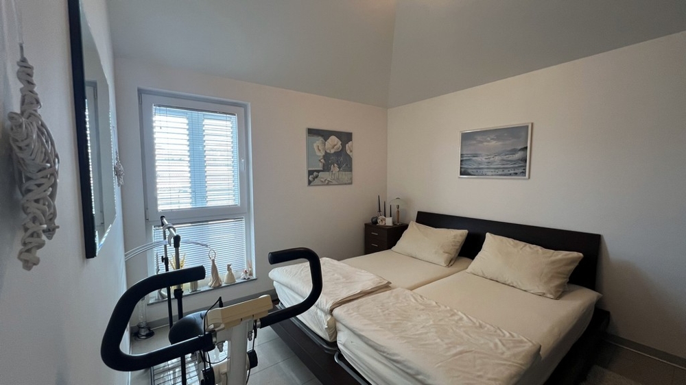 Sypialnia z dwoma pojedynczymi łóżkami, rowerem treningowym i minimalistycznymi meblami.