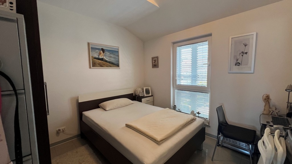 Sypialnia z podwójnym łóżkiem, prosto umeblowana, z oknem na ogród.