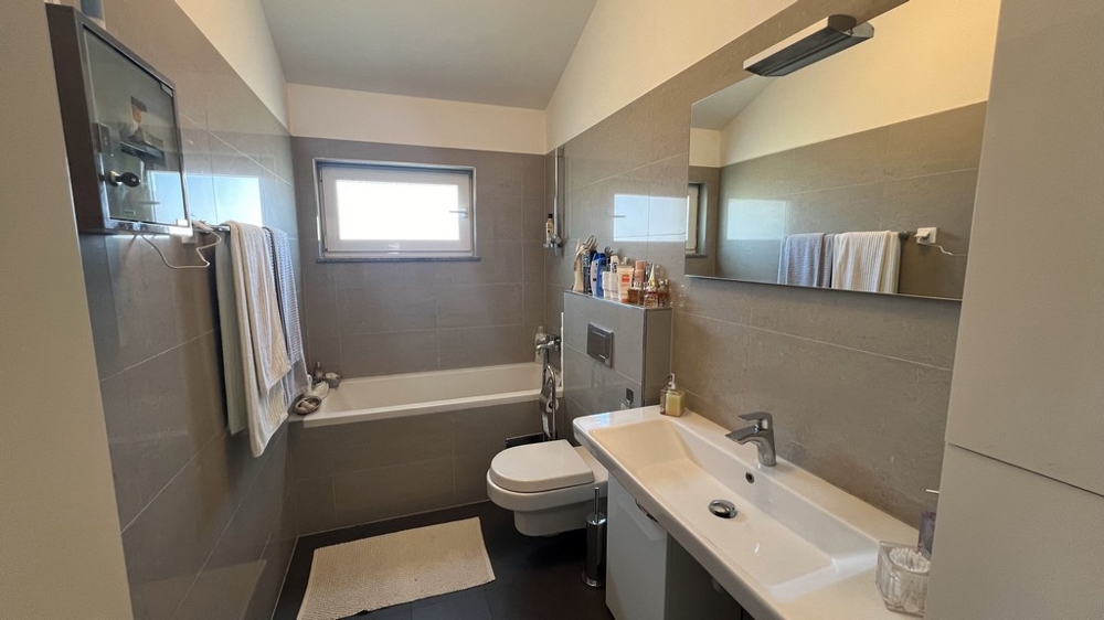 Nowoczesna łazienka z wanną, umywalką i toaletą, urządzona prosto i jasno.