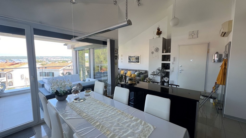 Jadalnia i kuchnia z nowoczesnymi meblami, duże okno wychodzące na taras z widokiem na morze.