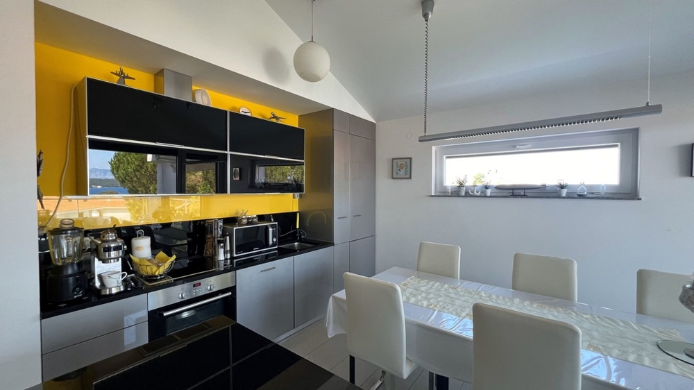 Nowoczesna kuchnia z czarnym blatem i żółtą tylną ścianą, sąsiadująca z jadalnią.