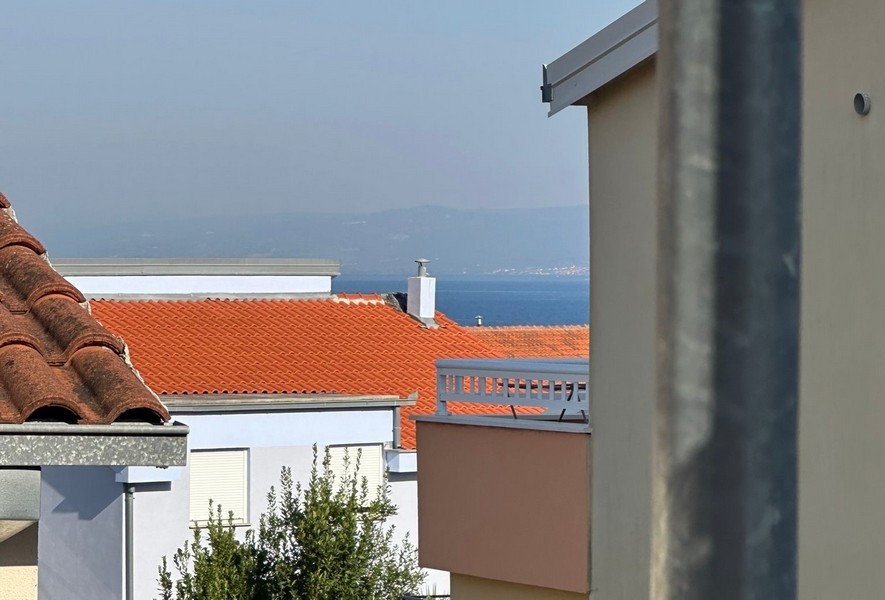 Zbliżenie na dachy pokryte czerwoną dachówką z niewielkim przebłyskiem morza w oddali