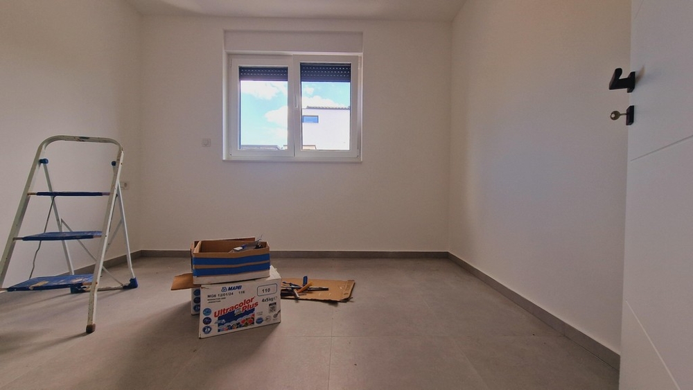 Nieumeblowany pokój z szarą podłogą, drabiną i ruchomymi pudłami