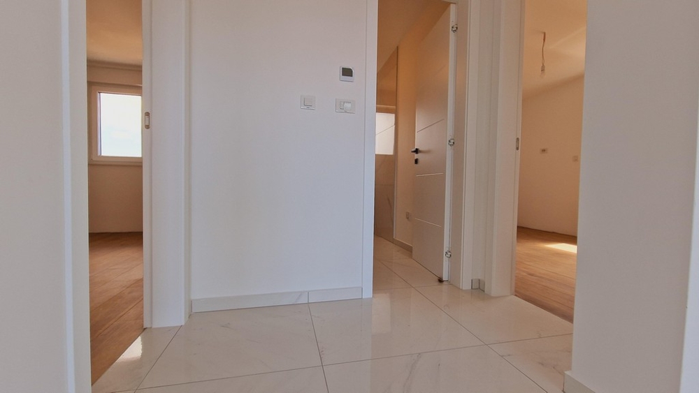 Przedpokój mieszkania z białymi płytkami i kilkoma drzwiami do różnych pokoi