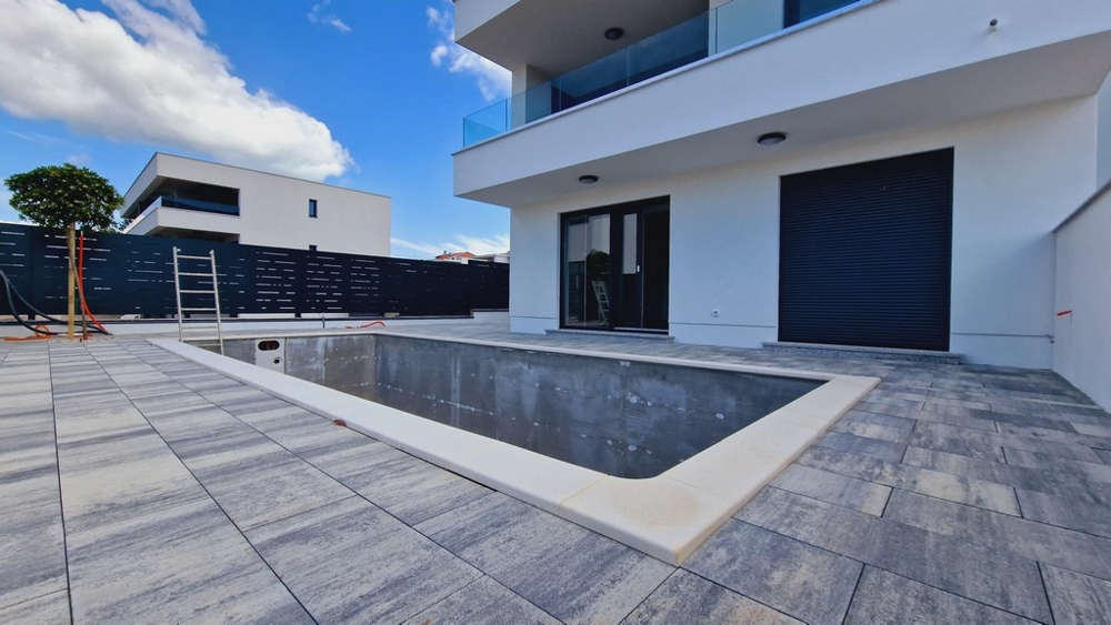 Teren basenu w budowie przed nowoczesnym budynkiem ze szklanymi balkonami i dużymi tarasami