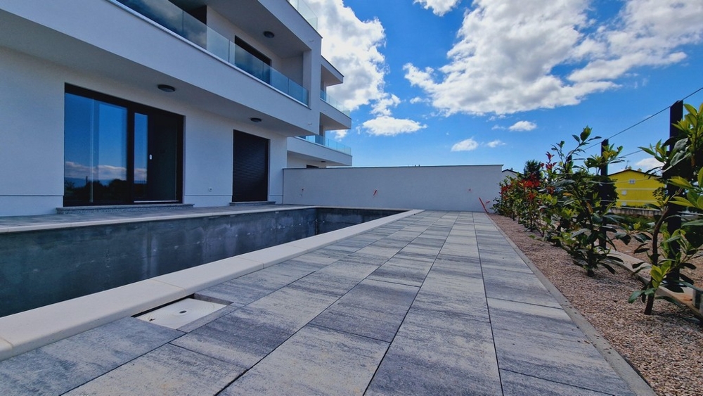 Na zewnątrz nowoczesny budynek z niekompletnym basenem i ogrodami