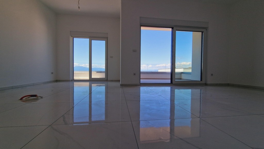 Wnętrze mieszkania z dużymi oknami i błyszczącą podłogą wyłożoną kafelkami, widok na taras i morze