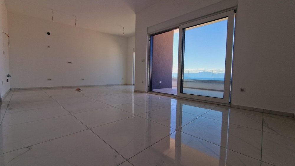 Część dzienna mieszkania z dużymi oknami i błyszczącymi podłogami wyłożonymi kafelkami, wyjściem na taras z widokiem na morze