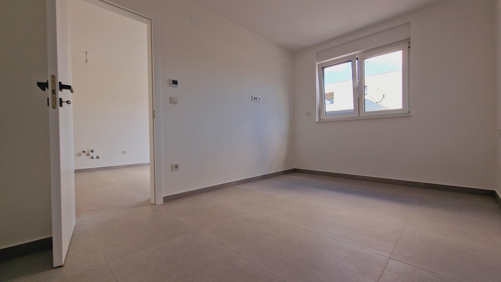 Mały, jasny pokój z podłogą wyłożoną szarymi kafelkami i oknem