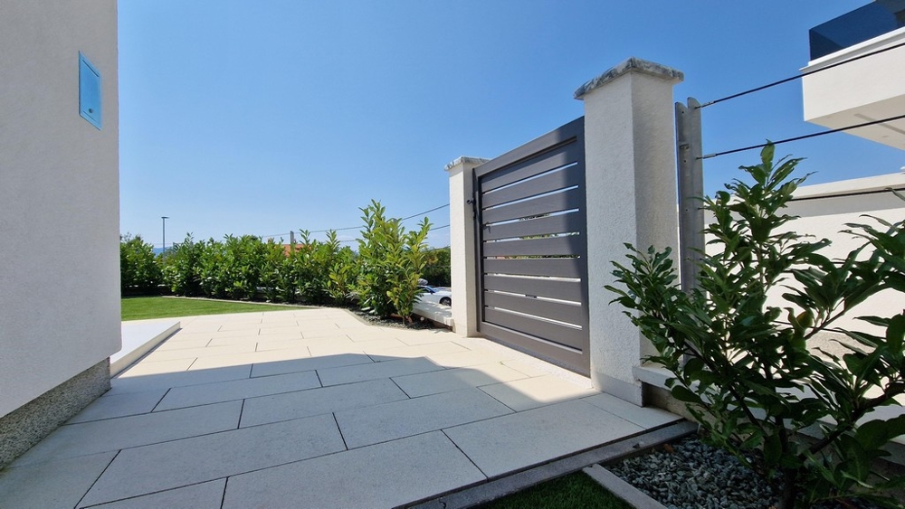 Brama wjazdowa do nowoczesnego budynku z utwardzonym podjazdem i zielenią.