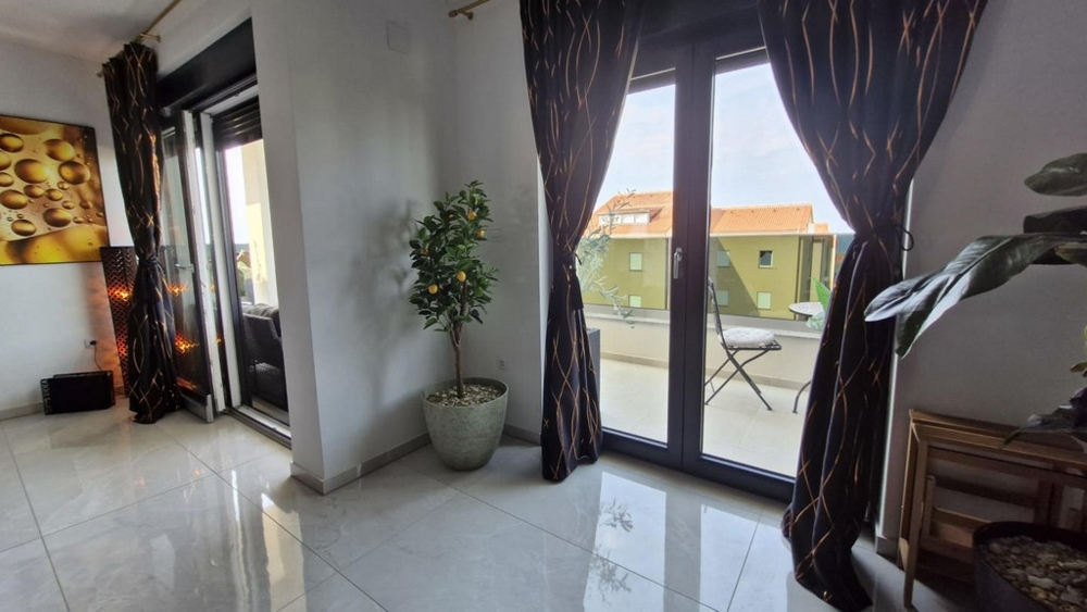 Widok na dwoje drzwi balkonowych z zasłonami, w rogu roślina doniczkowa