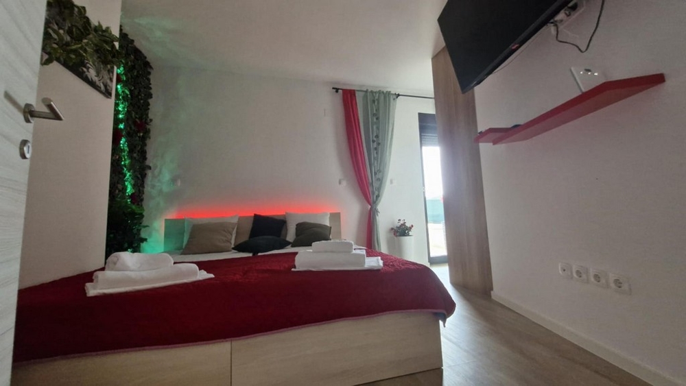 Sypialnia z czerwoną narzutą, dekoracyjnym tłem i telewizorem na ścianie