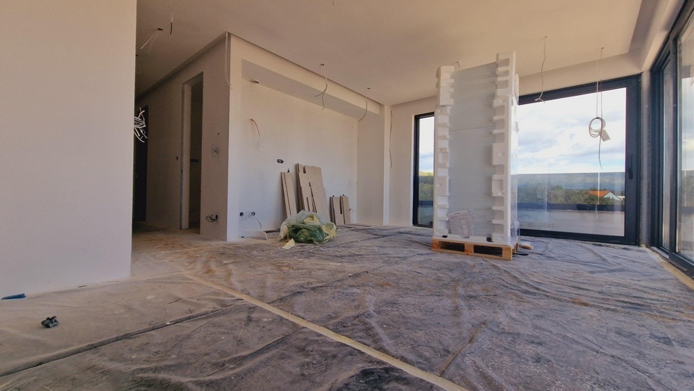 Powierzchnia mieszkalna nowego budynku w fazie wykończenia, z widokiem na duże przeszklenia i otaczającą przyrodę.