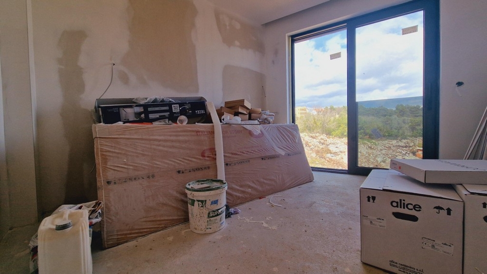 Niedokończony pokój z materiałami budowlanymi i dużym oknem z widokiem na krajobraz.