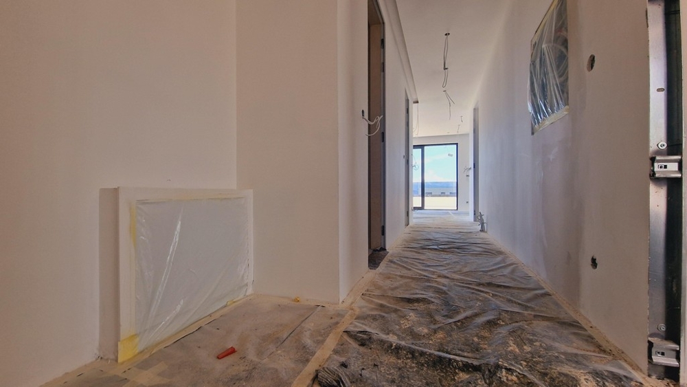 Przedpokój nowego budynku w fazie budowy z widokiem na taras na końcu korytarza.