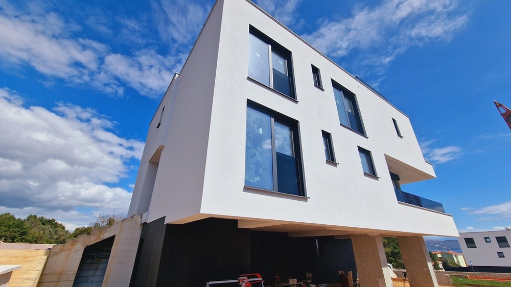Widok zewnętrzny nowoczesnego nowego budynku z wyraźną, białą fasadą i kilkoma dużymi oknami.