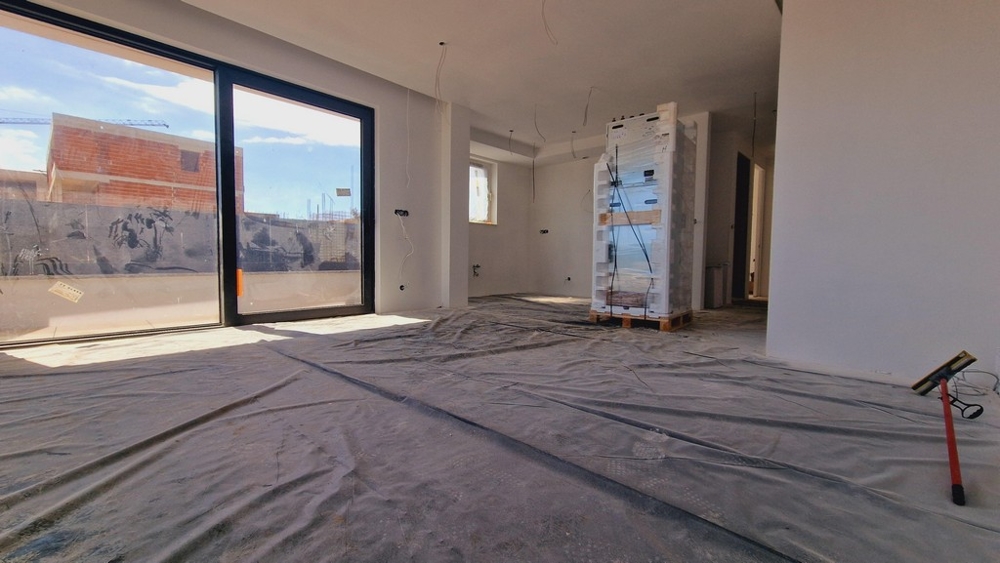 Widok wnętrza nowego mieszkania z dużymi frontami okien i wyraźnym widokiem na taras i okolicę.