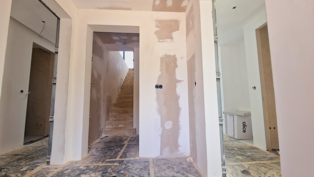 Klatka schodowa i korytarz w budowie z widocznymi ścianami osłonowymi i otwartymi kablami.