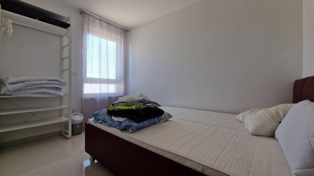 Sypialnia z minimalistycznymi meblami, oknem i otwartym miejscem do przechowywania ubrań.