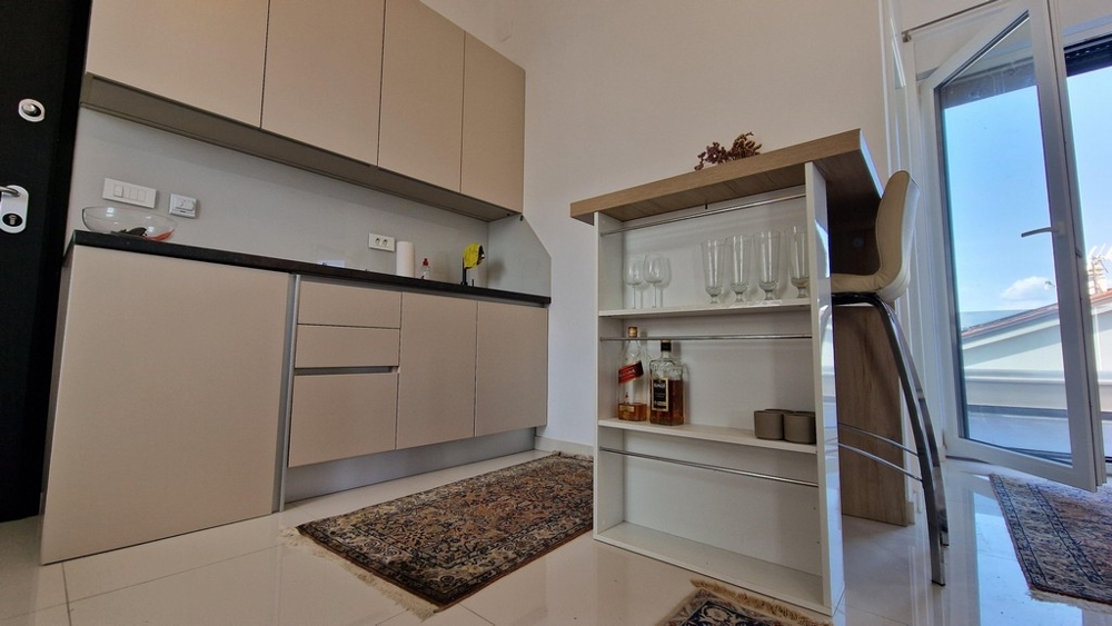 Mały, nowoczesny aneks kuchenny ze zintegrowanymi półkami i stołkami barowymi, wyjściem na taras.