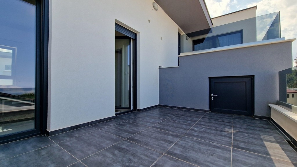 Nowoczesny taras z szarymi płytkami, szklanymi balustradami i dostępem do mieszkania.