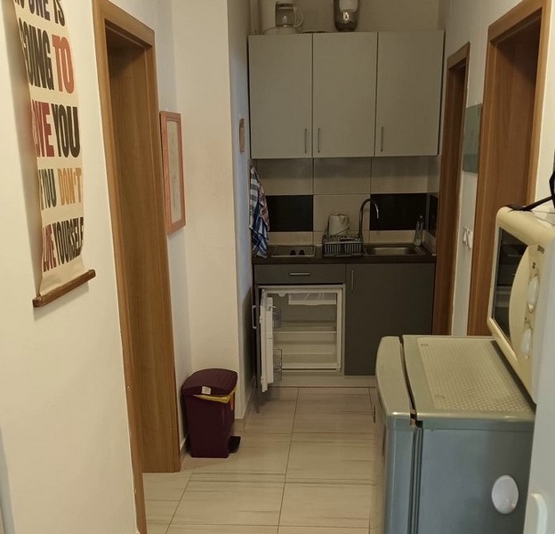 Mała kuchnia z szarymi szafkami, małą lodówką i kuchenką mikrofalową na korytarzu.