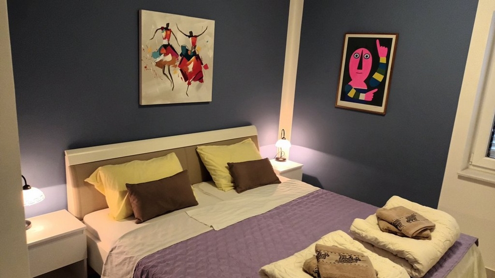 Sypialnia z podwójnym łóżkiem, fioletową kołdrą i dwoma obrazami na ścianach.