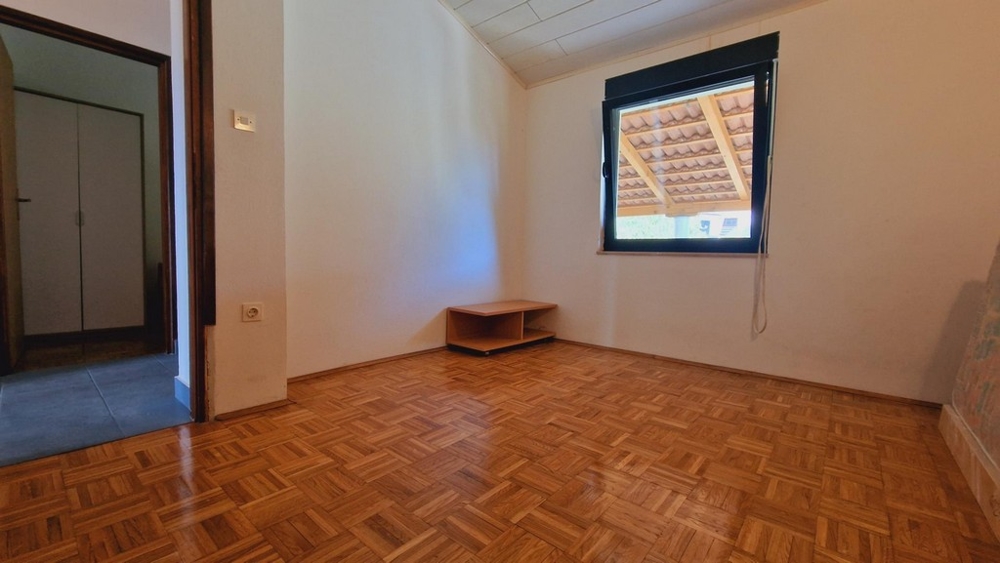 Pusta sypialnia z dużym oknem, prostymi meblami i drewnianą podłogą.