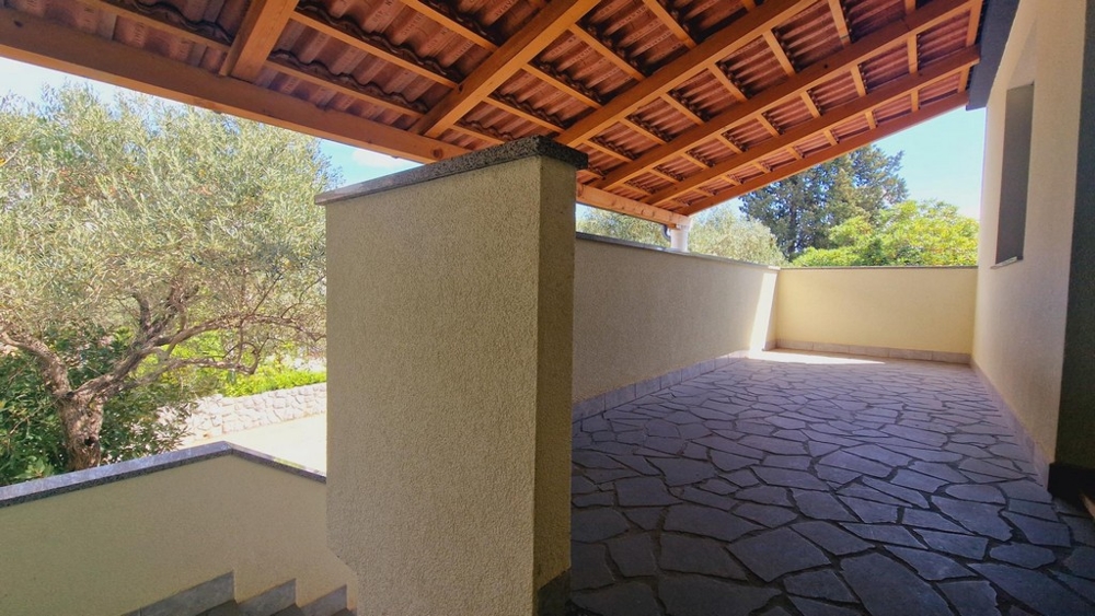 Zadaszony teren zewnętrzny z kamienną podłogą, widokiem na drzewa i przyrodę.