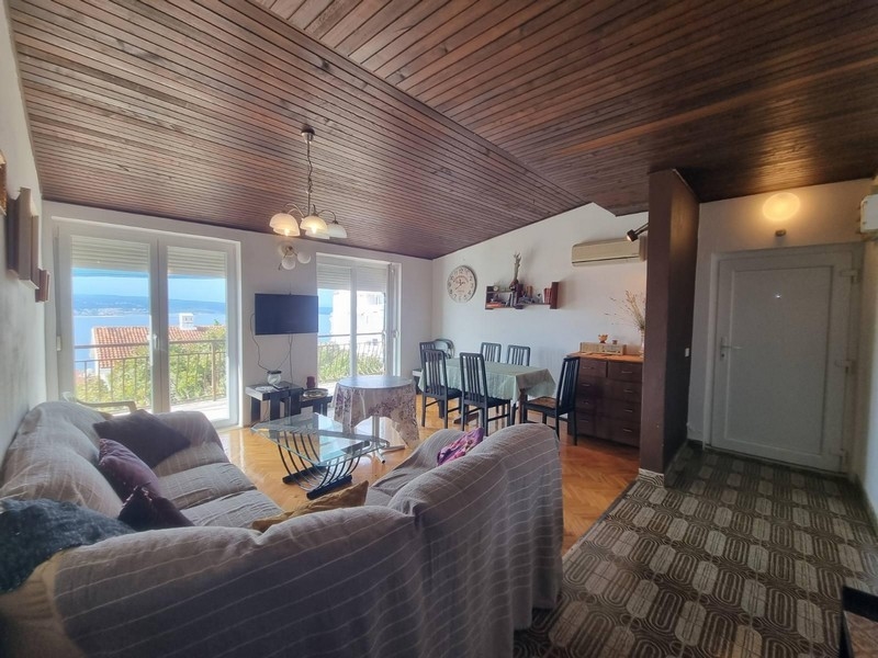 Pokój dzienny z wyjściem na balkon, drewnianym stropem i widokiem na morze.