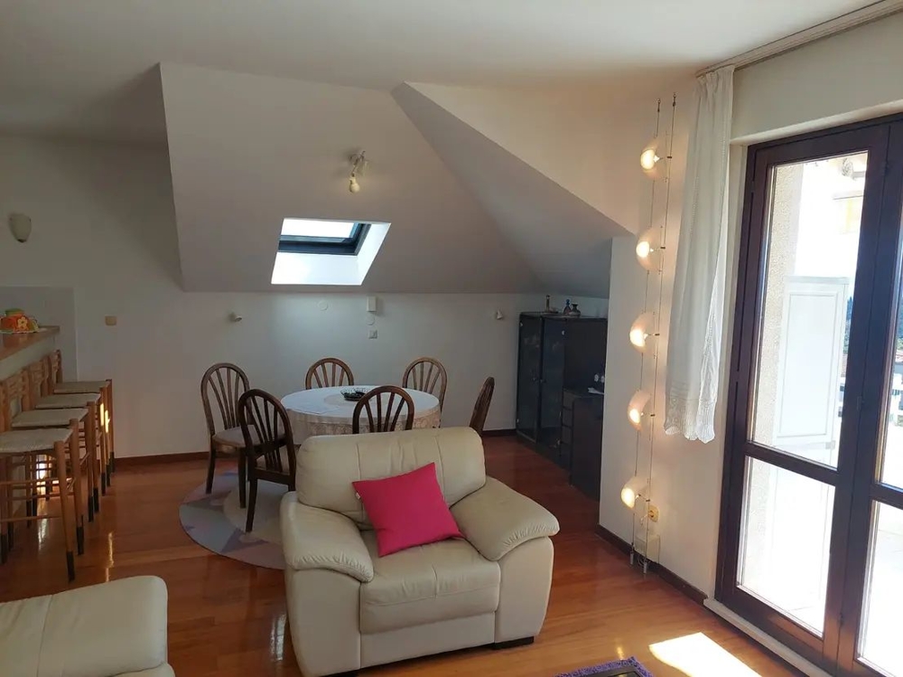 Stół w mieszkaniu na poddaszu, duże okna i stołki barowe przy blacie kuchennym