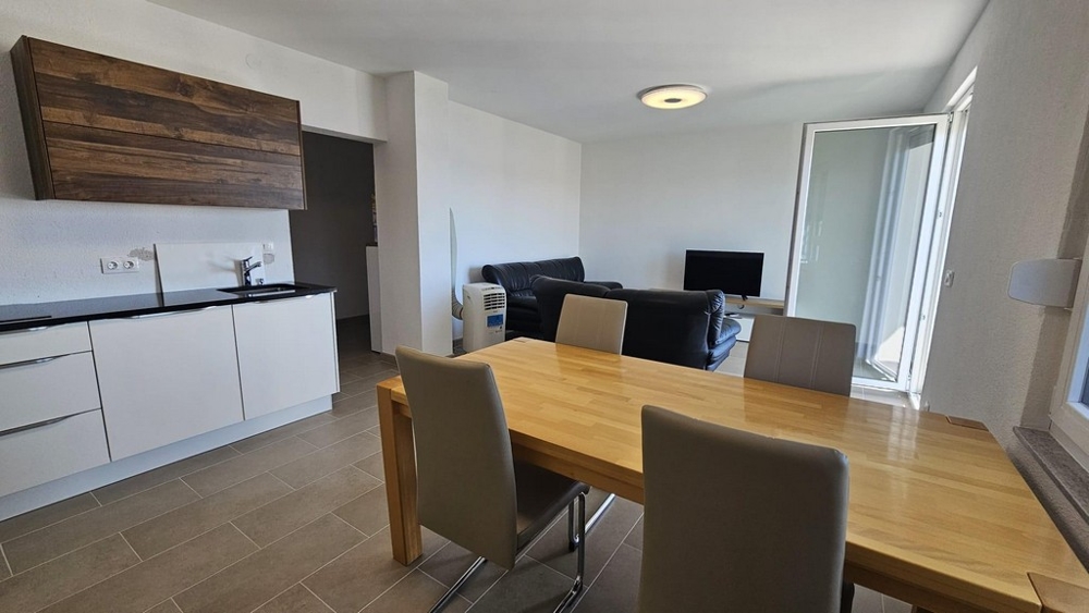 Nowoczesna otwarta kuchnia z drewnianymi elementami, jadalnią i częścią wypoczynkową z wyjściem na balkon.