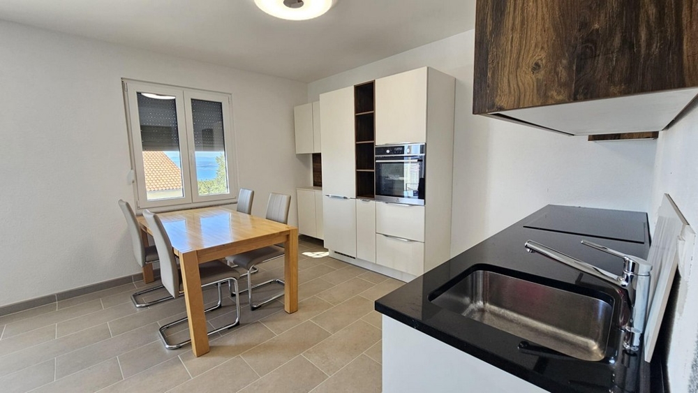 Jasna kuchnia ze stołem jadalnym, nowoczesnym sprzętem AGD i oknem z widokiem na morze.