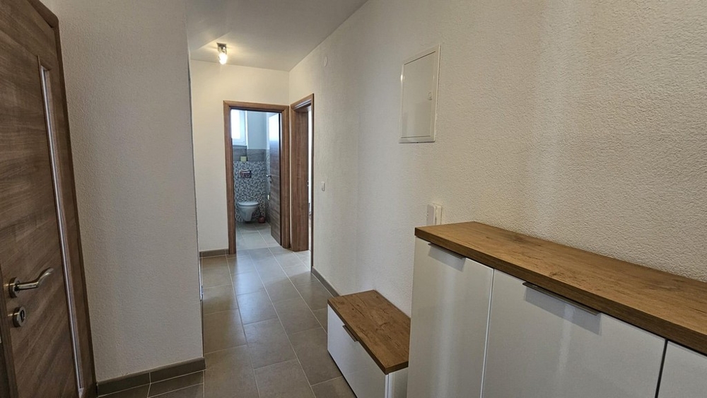 Przedpokój prowadzący do łazienki z podłogą wyłożoną kafelkami i akcentami drewna.