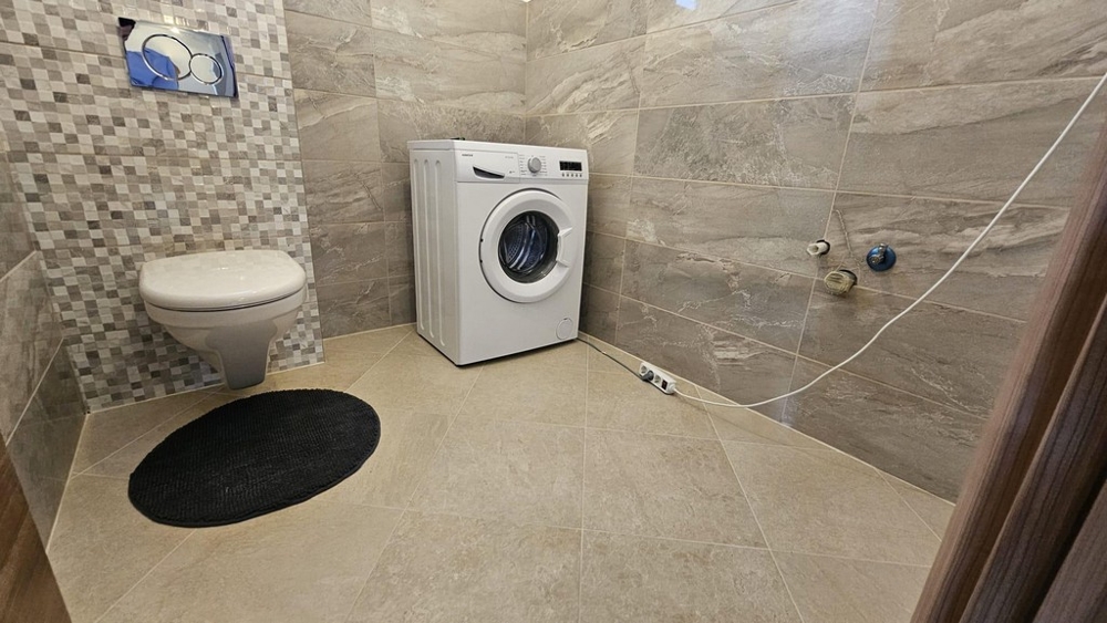 Łazienka z pralką, toaletą i ścianami wyłożonymi kafelkami.