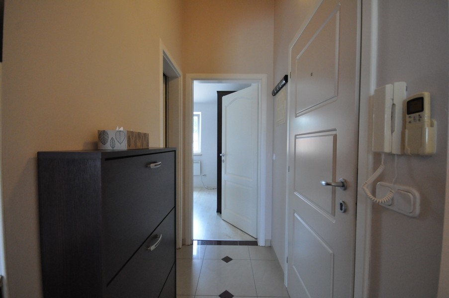 Przedpokój z białymi drzwiami, ciemną szafką i domofonem na ścianie, dostęp do różnych pomieszczeń