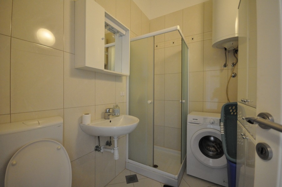 Łazienka z prysznicem, umywalką, toaletą i pralką, ściany i podłoga wyłożone jasnymi kafelkami