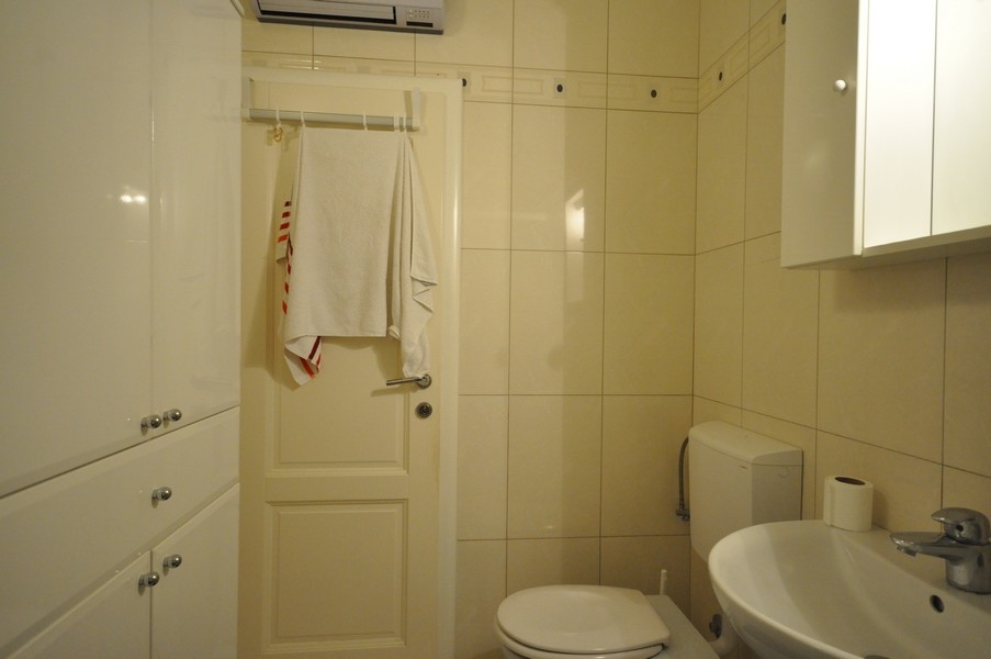 Łazienka z WC, umywalką, wieszakiem na ręczniki na drzwiach, jasnymi płytkami, nowoczesnym wyposażeniem