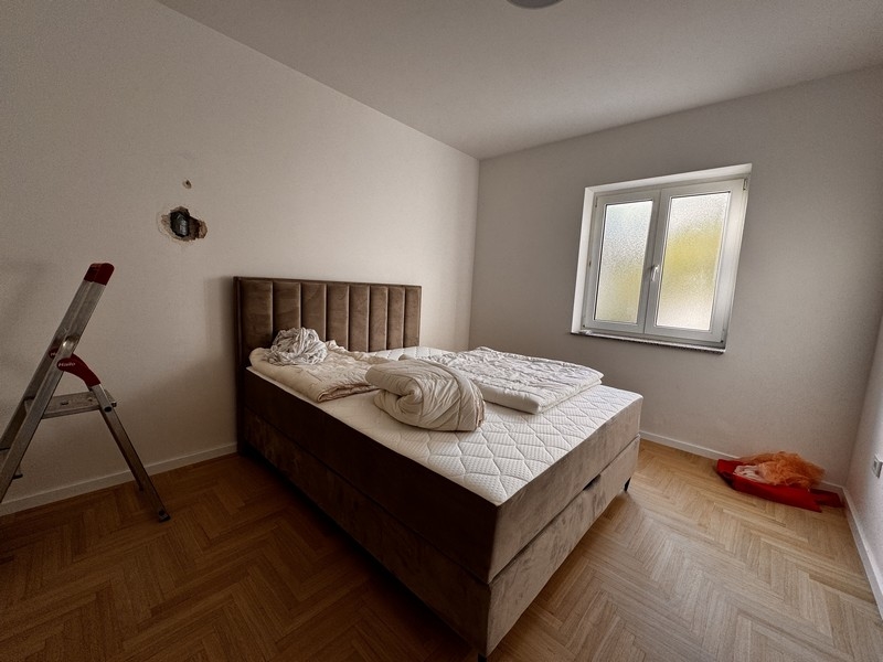 Sypialnia z dużym tapicerowanym łóżkiem, białymi kocami i małym oknem